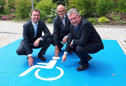 Landrat Matthias Dießl, Behindertenbeauftragter des Landkreises Fürth Stephan Beck und Steins Erster Bürgermeister Kurt Krömer zeigen auf einen der neu gestalteten Behindertenparkplätze